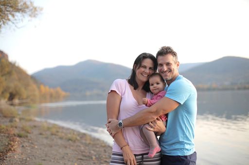 A cheerful family with a little child standing near a lake surrounded by hills under the sunlight