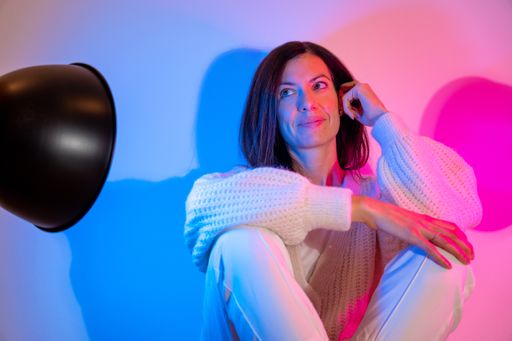 A smiling young Caucasian woman wearing a knitted sweater with a blue and a pink spotlight