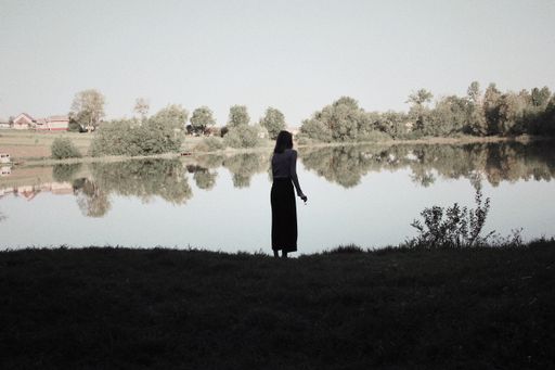 A silhouette of a tall female standing near a reflecting lake during cold weather and holding a flower