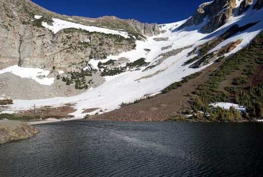 A scenic view of a lake against a snowy slope of a mountain on a sunny day