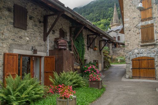 A scenic view of antique stone buildings surrounded by green plants and flowers in Isere, France