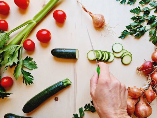 A top view of a female hand cutting a cucumber with a knife