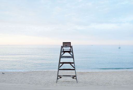 A close shot of a lifeguard's chair on a beach shore with a cloudy sky in the background