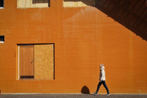 A beautiful shot of a person with a white jacket walking on a sidewalk near an orange building at daytime