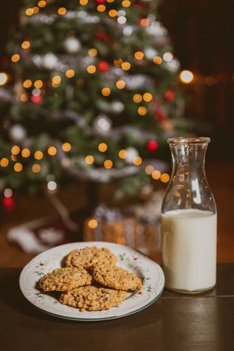 A vertical shot of a jar of milk and a plate of homemade cookies near a Christmas tree