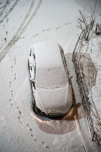 A vertical aerial view of a car covered in snow and footsteps around it