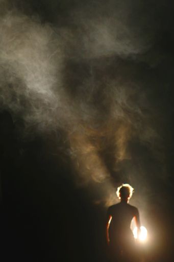 A back shot of a male blocking the sun with a long exposure of a
 smoky dark sky