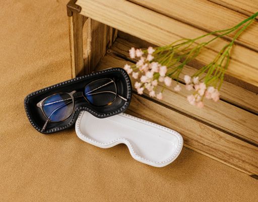A closeup shot of eyeglasses and black and white cases decorated with white flowers on a wooden surface
