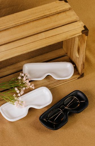 A vertical shot of eyeglasses and black and white cases decorated with white flowers on a wooden surface