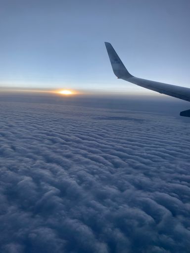A vertical shot of an airplane wing above the clouds during sunset