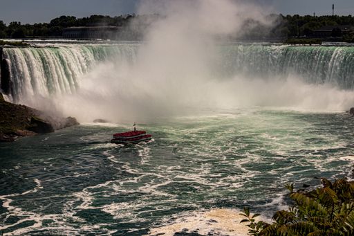 A beautiful wide shot of a large waterfall with a tourist cruise ship sailing near it