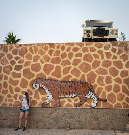 A young girl in front of the wall with an old wrecked Land Rover SUV on the top