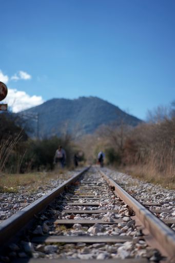 A vertical shot of an empty railroad surrounded by people in Peloponnese on a sunny day