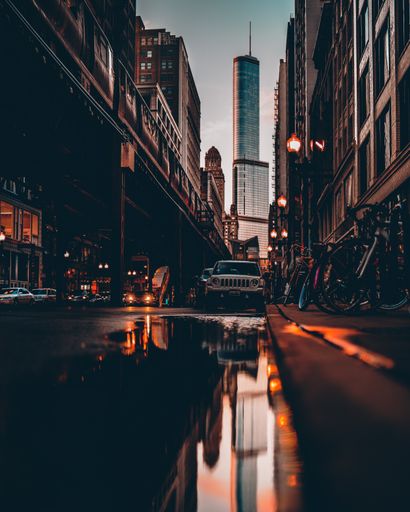 A vertical shot of reflection of vehicles on a water puddle on the street with bicycles parked near skyscrapers