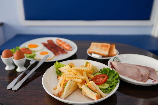 A breakfast table with club sandwich, French fries, ham, boiled eggs, omelet, toasts