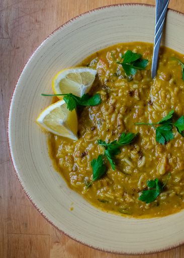 A vertical high angle shot of a plate of vegetable soup with parsley and lemon on a wooden table