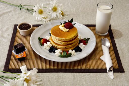 A breakfast containing pancake with strawberries, blueberries  and a cup of milk