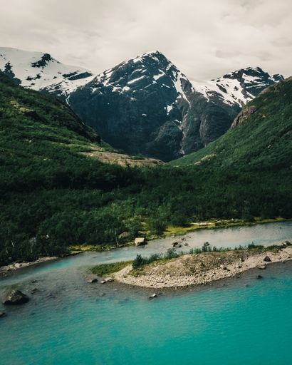 A vertical shot of a river with hills and snowy mountains in the background