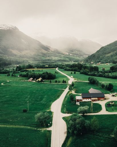 A vertical shot of a small rural building in a green field with snowy mountains in the background