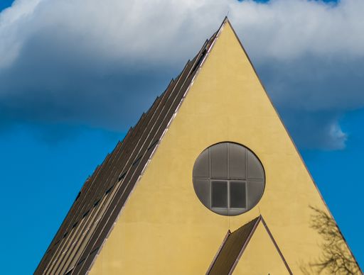 A closeup shot of the yellow triangle roof of a building with a round window