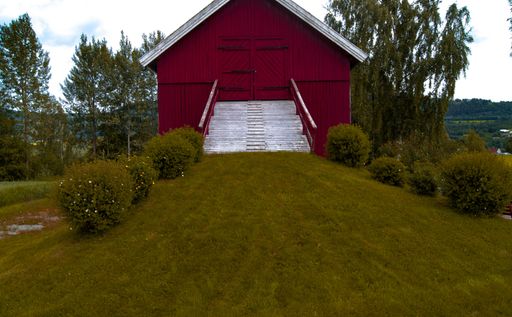 A view of a rural building in a green field with forests in the background