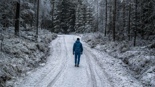A man walking through a snowy road in the middle of a forest