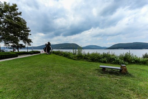 A beautiful waterfront landscape field with an empty bench in Peekskill, New York on a cloudy morning in late summer