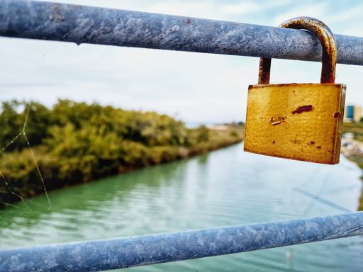 A golden padlock hooked on the railing of the bridge over the river