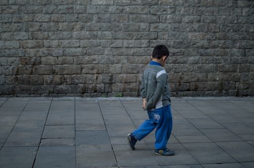 the child is on his back, you cannot see his face and the background is a stone wall