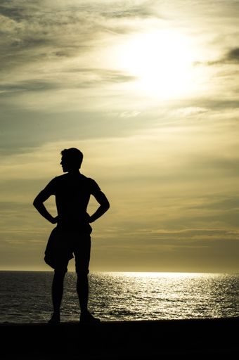 A vertical shot of a man silhouette near the ocean with cloudy skyline
