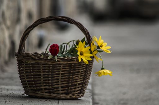A closeup shot of a rose and yellow daisies in the basket on a stone surface