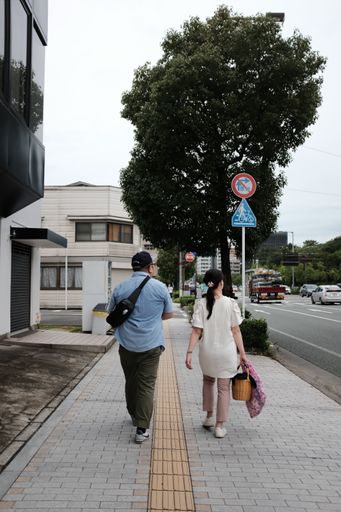 A vertical shot of a male and female walking along a sidewalk with houses and trees by the street