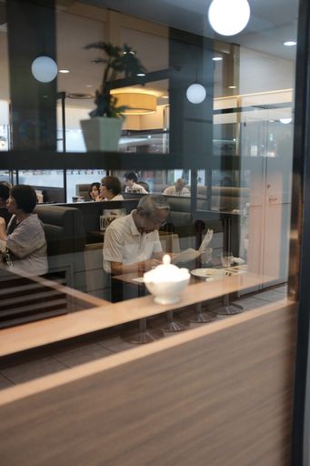 A vertical selective closeup shot of a male sitting in a cafe near other people reading a newspaper