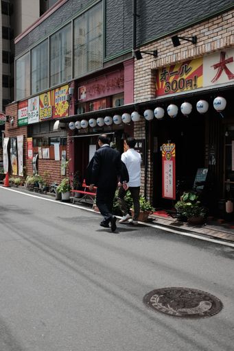 A vertical shot of two males walking along a road near street shops