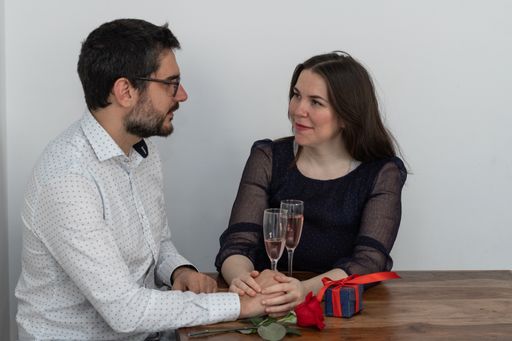 A Caucasian couple having a romantic date with glasses of pink champaign, a red rose, and a candle
