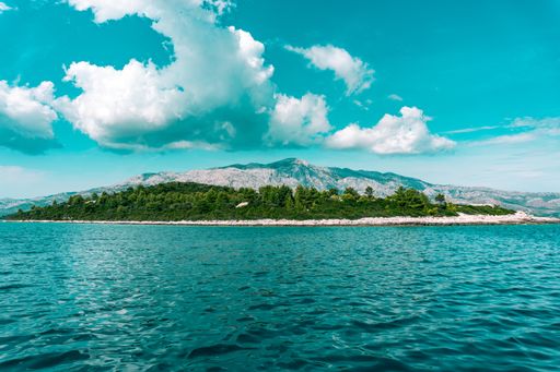 A mesmerizing view of a far green island and shiny blue wavy water against a cloudy blue sky