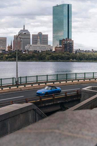vertical shot of blue car driving in front of the Boston city skyline.