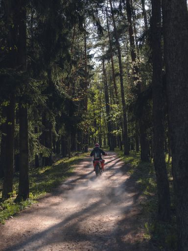 A vertical shot of a man with helmet riding red motorbike in the forest