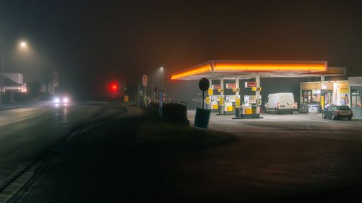 An illuminated Shell gas station in a dark and foggy night