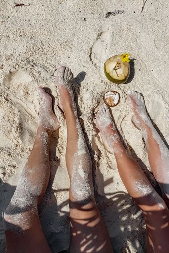 A top view of human legs of a couple covered with sand relaxing on a tropical sandy beach