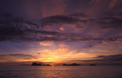 A wide shot of a sea with cliff in the distance under a purple sky during sunset