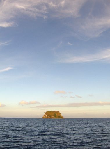 A vertical shot of an islet on the body of a sea under a blue sky