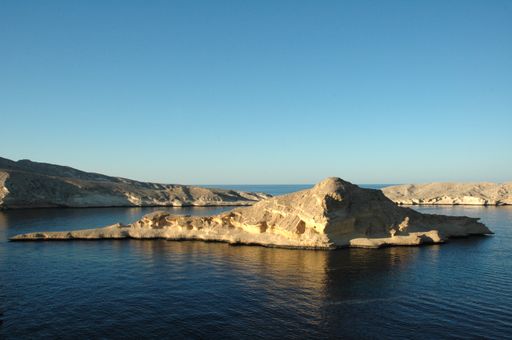 A wide shot of rock formations on the body of water under a clear blue sky