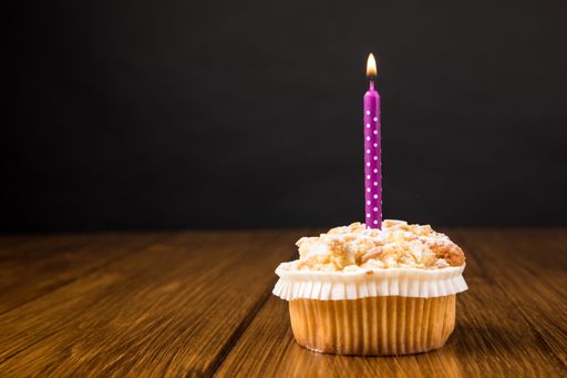 A muffin with a purple burning candle on a dark wooden background