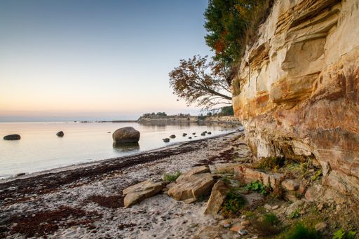 Sunset colored scenic view to the calm sea bay and tall cliff consist of sandstone and limestone sedimentation layers