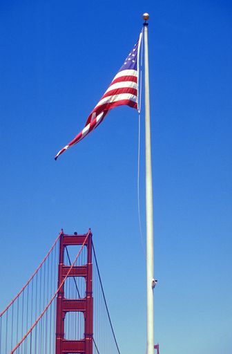 A vertical shot of the United States of America or USA flag on a flagpole on the background of the Golden Gate Bridge