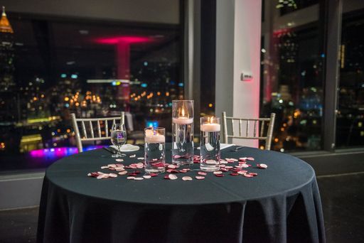 A romantic date table decorated with candles and rose petals with a cityscape in the background
