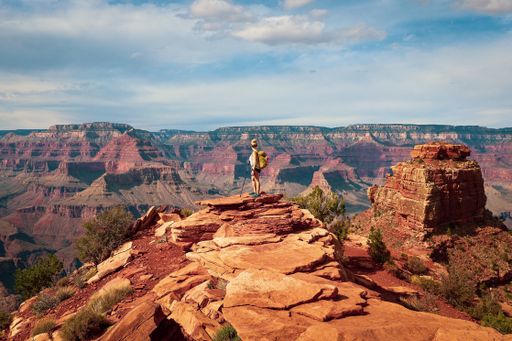 A female tourist standing on a rocky outcrop and admiring the view of the Grand Canyon in Arizona