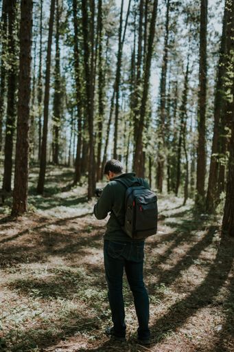 A vertical shot of a tourist man in a backpack in the forest