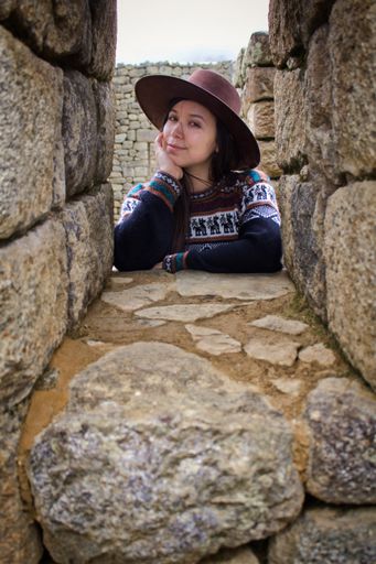 A closeup shot of a pretty Hispanic girl looking through the stone window at the lost old Inca city Machu Picchu